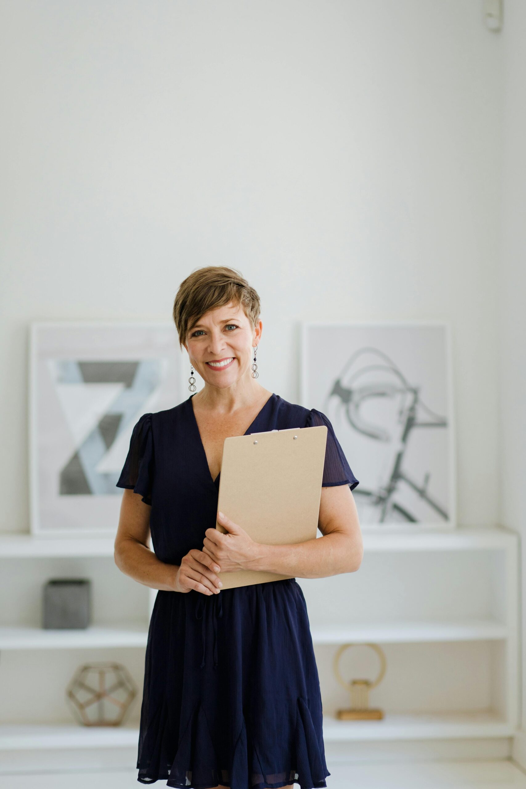Woman with short hair holding a clipboard in a minimalist indoor setting.